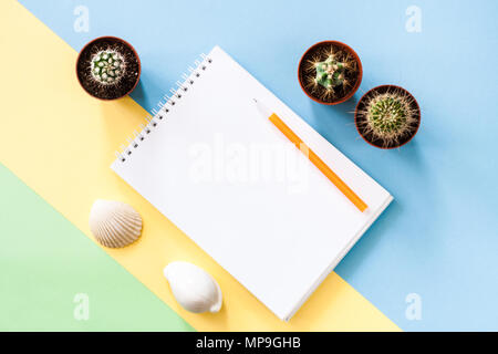 Piano di composizione dei laici con il blocco note, tre verdi cactus, due conchiglie sul colore pastello giallo-blu-verde dello sfondo. Foto Stock