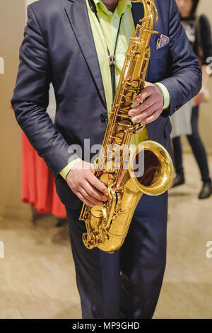 Il musicista suona il sassofono prestazioni a un concerto nel centro commerciale del negozio di abbigliamento per donna in vacanza Foto Stock