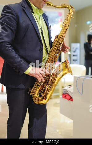 Il musicista suona il sassofono prestazioni a un concerto nel centro commerciale del negozio di abbigliamento per donna in vacanza Foto Stock