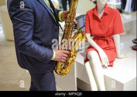 Il musicista suona il sassofono prestazioni a un concerto nel centro commerciale del negozio di abbigliamento per donna in vacanza Foto Stock