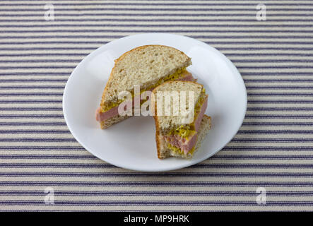 Un parzialmente mangiato salumi conserve di carne in sandwich di pane di grano sulla cima di un blu tovaglia a righe. Foto Stock