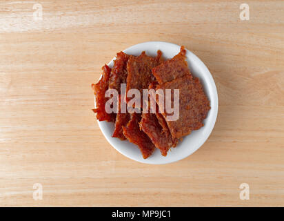 Vista dall'alto di una piccola ciotola bianco riempito con carne di maiale marinato a scatti su una tavola di legno. Foto Stock