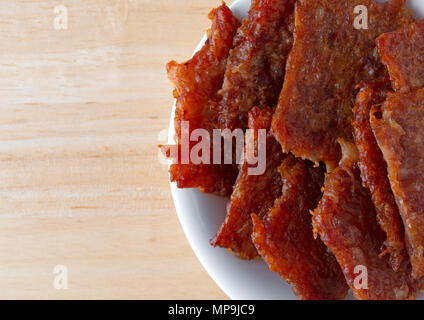 Top vista ravvicinata di una piccola ciotola bianco riempito con carne di maiale marinato a scatti su una tavola di legno. Foto Stock