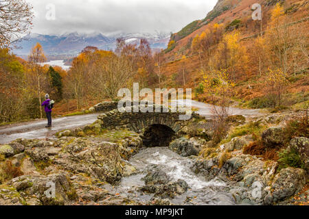 Escursionista persona ammira Ashness Bridge nel Parco Nazionale del Distretto dei Laghi Campagna, Inghilterra, con Derwent Water e Cat campane montagne sullo sfondo Foto Stock