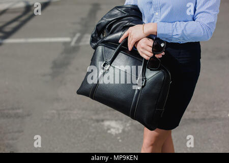 Sezione mediana di imprenditrice con borsa nera in piedi in città Foto Stock