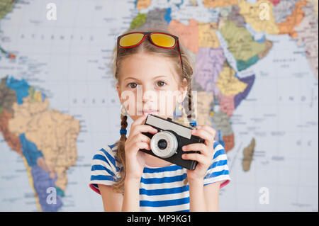 Graziosa bambina in striped sailor camicia e occhiali da sole con vintage camere in mani sulla mappa del mondo sullo sfondo Foto Stock