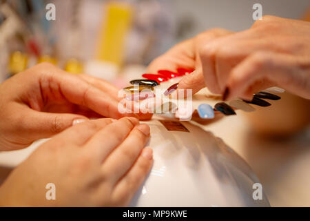 Close-up di una estetista e clienti di sesso femminile mani tenendo i campioni e la scelta di colori le unghie al salone di bellezza. Foto Stock