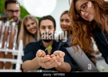 Università collega biologi tenendo un giovane pianta nel suolo in mani e controllare la qualità del campione. Foto Stock