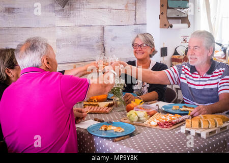 4 seniors a pranzo la tostatura con vino e celebrare insieme a Brindisi. Gli uomini hanno la barba e le donne hanno occhiali Foto Stock