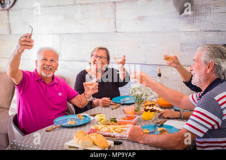 Coppie Senior tenendo selfie a casa la tostatura del vino rosso e mangiare il pranzo pasto - vecchi amici divertendosi con le nuove tendenze della tecnologia Foto Stock