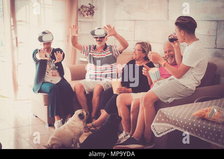 Persone di età mista facendo parte a casa con gli occhiali di protezione auricolare. un sacco di divertimento e pop corn. due belle pugs sul terreno in attesa di cibo Foto Stock