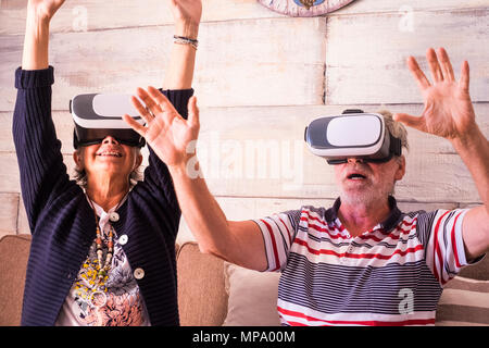 Di età compresa tra i senior l uomo e la donna che gioca con gli occhiali di protezione auricolare a casa sedersi sul divano. roller coaster sensazione Foto Stock