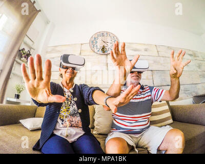 Paio di senior a giocare a roller coaster con la realtà virtuale cuffia seduto sul divano di casa. La felicità per pensionati uomo e donna con goggle g Foto Stock