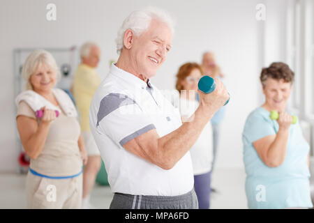 Uomo vecchio esercizio bicipite utilizzando il manubrio durante le lezioni di fitness Foto Stock