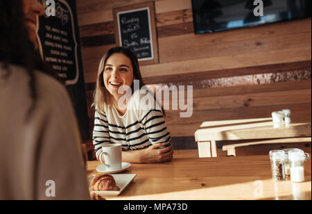 Donna sorridente seduto in un ristorante a parlare con il suo amico. Amici seduti in un caffè con caffè e snack sulla tabella. Foto Stock