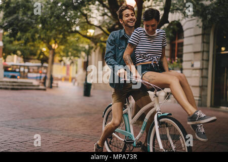 Giovane uomo e donna in sella ad una bicicletta in città. Coppia felice su una bicicletta in città. Foto Stock