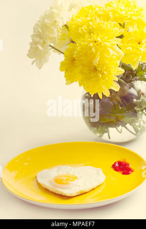 La prima colazione. Uova fritte in un a forma di cuore bouquet di crisantemi vicino Foto Stock