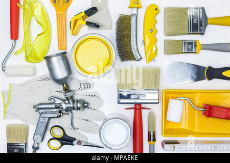 Pennelli, rulli, lattine, guanti, occhiali di protezione e la pistola a spruzzo su bianco scrivania in legno Foto Stock