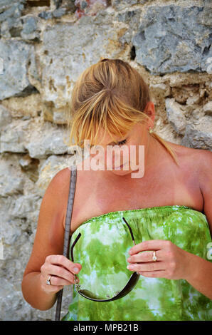 Femmina bionda guardando verso il basso in corrispondenza di occhiali da sole Foto Stock