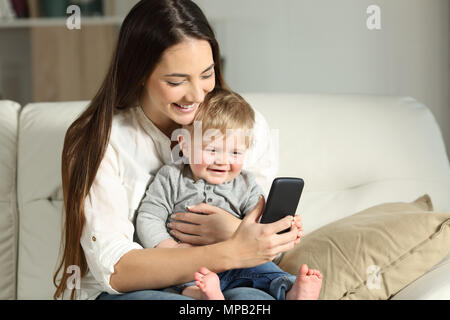 La madre e il bambino gioca con uno smartphone seduta su un divano nel salotto di casa Foto Stock