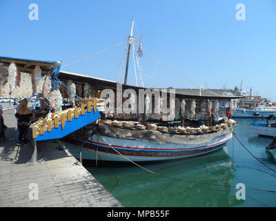 I turisti sfogliando la merce su un greco barca da pesca trasformati in un negozio di souvenir al porto di Rodi, Grecia. Foto Stock