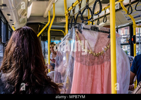 Donna recuperati un abito rosa con paillettes (paillettes) avvolto in un lavaggio a secco Servizio lavanderia sacchetto di plastica, appeso sul corrimano su una città urban bus pubblico. Foto Stock