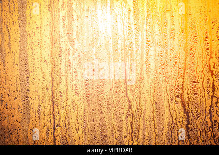 Sole brillante splendenti attraverso il vetro della finestra. Sunrise in giallo arancione bruno tinte. Le gocce di acqua sulla superficie del vetro. Uno sfondo ideale per le illustrazioni e collage. Foto Stock