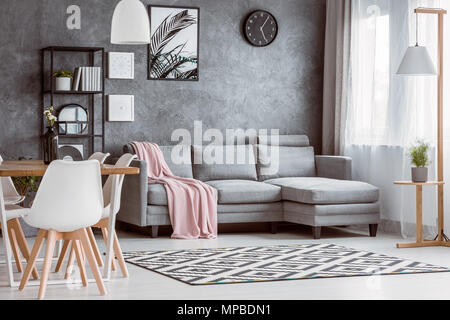 Tavolo da pranzo con sedie bianche in uno spazioso soggiorno con il rosa coverlet sul divano grigio Foto Stock