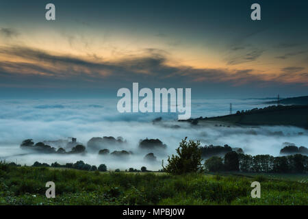 Denso e pesante, laminazione, bassa giacente nube di sera, nebbia o foschia sopra Askerswell village, Dorset nella campagna inglese e al tramonto visto dalla collina A35. Foto Stock