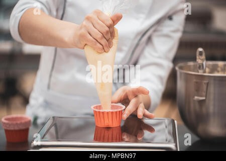 Chiudere fino a mani dello chef con il sacchetto di pasticceria la spremitura di crema sulle tortine Foto Stock