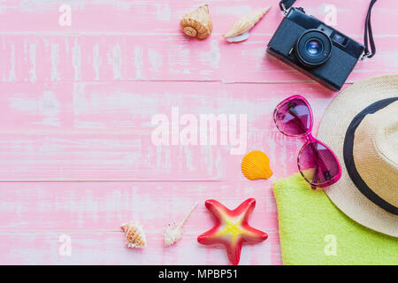 Spiaggia accessori compresi occhiali da sole, crema solare, cappello beach, shell, stelle marine e fotocamera retrò sul rosa chiaro pastello sullo sfondo di legno per l'estate holi Foto Stock