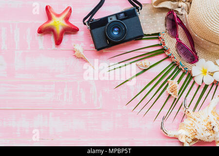 Spiaggia accessori compresi occhiali da sole, crema solare, cappello beach, shell, noce di cocco verde foglie Palm tree e fotocamera retrò sul rosa chiaro pastello torna in legno Foto Stock