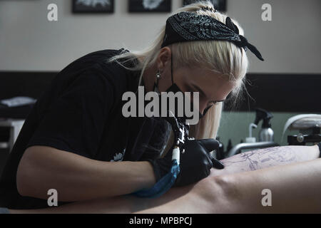 Artista che indossa maschera tatuando sulla coscia della donna presso lo studio d'arte Foto Stock