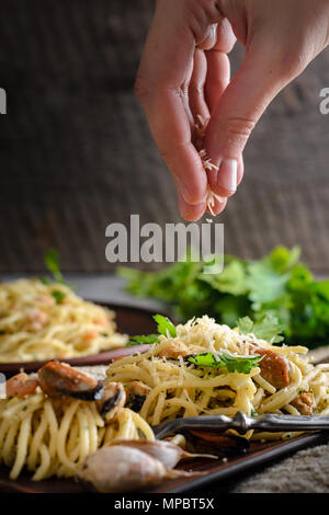 Una donna irrora un formaggio parmigiano pasta di gamberi e cozze in una salsa cremosa. Cucina italiana Foto Stock