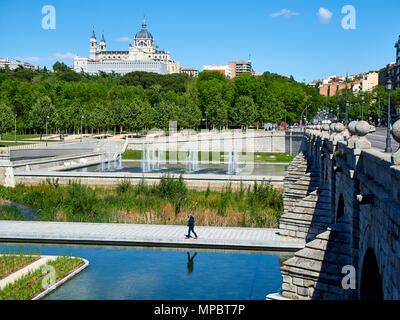 Puente de Segovia ponte che attraversa i giardini di Madrid Rio alla giornata di primavera con la cattedrale di Almudena in background e un uomo a piedi in primo piano. Foto Stock