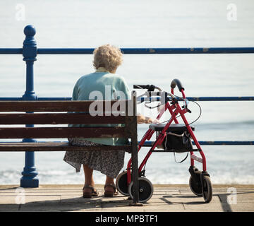 Anziani donna seduta su un banco da lavoro che si affaccia sul mare. Regno Unito Foto Stock