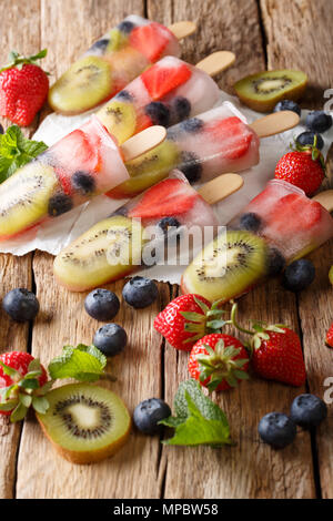 Una sana frutta intera Popsicles con bacche Fragole Kiwi closeup su legno tabella vintage verticale. Foto Stock