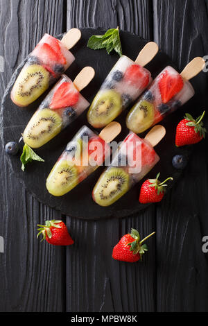Popsicles ghiaccio su un bastone di fragole, kiwi e mirtilli con la menta closeup sul tavolo. Verticale in alto vista da sopra Foto Stock