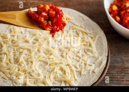 Realizzazione di quesadilla. Il cucchiaio di legno la diffusione del riempimento su tortilla cosparso con formaggio. Foto Stock