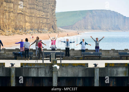 West Bay, Dorset, Regno Unito. 22 maggio 2018. Regno Unito Meteo. Un esercizio di gruppo sul molo Orientale con la mitica scogliere di arenaria dietro di loro, facendo il loro allenamento presso la località balneare di West Bay nel Dorset come godere di una calorosa soleggiata giornata di primavera. Credito Foto: Graham Hunt/Alamy Live News Foto Stock