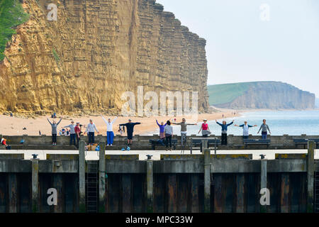 West Bay, Dorset, Regno Unito. 22 maggio 2018. Regno Unito Meteo. Un esercizio di gruppo sul molo Orientale con la mitica scogliere di arenaria dietro di loro, facendo il loro allenamento presso la località balneare di West Bay nel Dorset come godere di una calorosa soleggiata giornata di primavera. Credito Foto: Graham Hunt/Alamy Live News Foto Stock