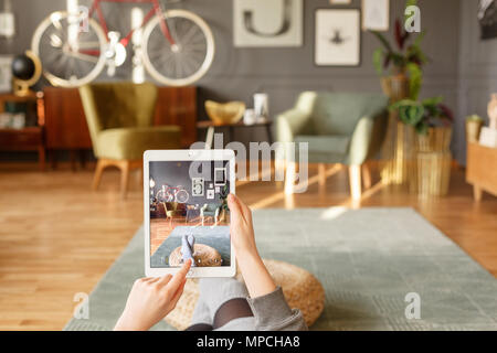 Una donna rilassante tenendo un tablet e utilizzando un touch screen mentre comodamente sdraiato su un tappeto verde in un piatto vintage interno con retro sfocata Foto Stock