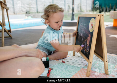 Un bambino diverte disegno su una lavagna. Un ragazzino scarabocchi con un gesso su una lavagna. Foto Stock