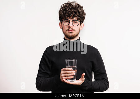 Giovane uomo in un studio, tenendo in mano un bicchiere d'acqua. Foto Stock