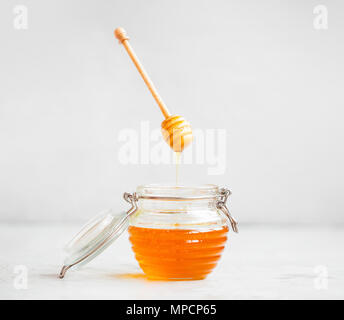 Materie organiche vaso di miele con bilanciere che galleggia in aria con miele di versare il vasetto di vetro Foto Stock