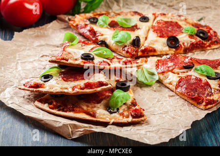 Fette di pizza salsiccia per pizza con olive servita su un foglio di carta Foto Stock