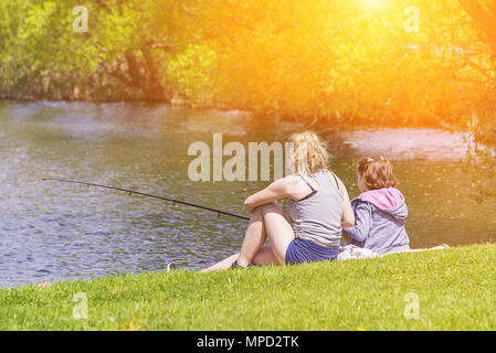 Madre e figlia di pesca in lago, nello stagno, seduto sulla riva verde Foto Stock