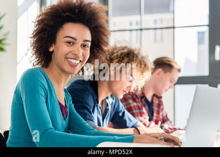 Ritratto di un allegro studente seduto alla scrivania in aula Foto Stock