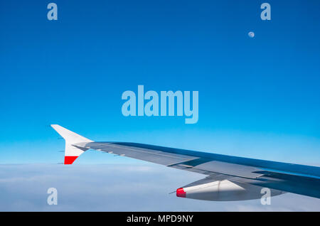 British Airways Airbus 319 ala piano scintillante di sole, visto dalla finestra del piano durante il volo con il cielo azzurro in UK e visibile della luna Foto Stock