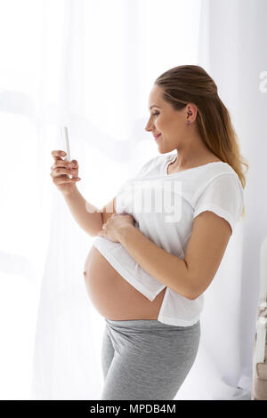 Felice donna incinta prendendo selfie Foto Stock